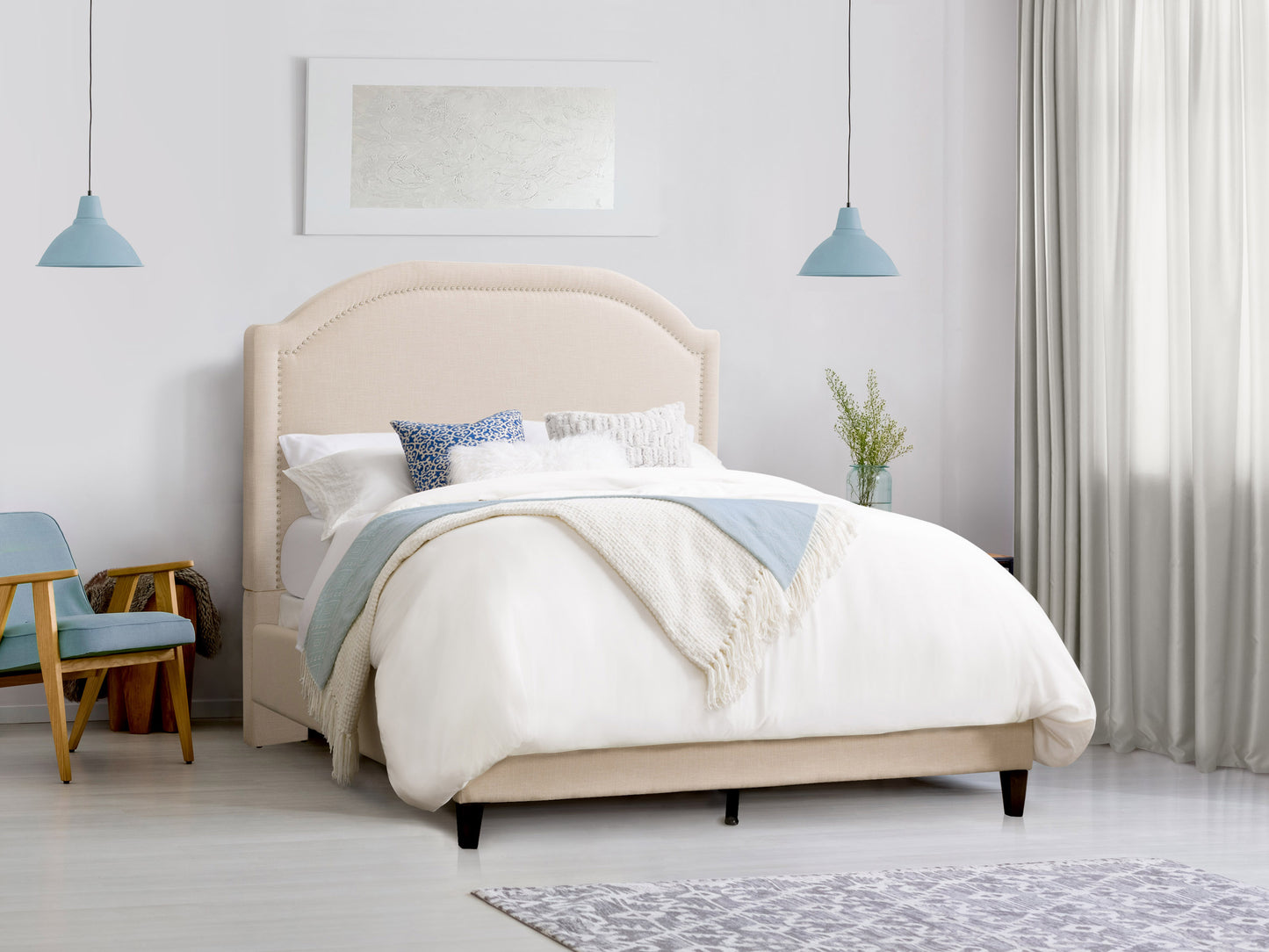 Gray upholstered double bed with tufted headboard, wooden legs, and a modern design. The bed is dressed with white linens and complemented by a cozy gray throw blanket and two matching pillows.