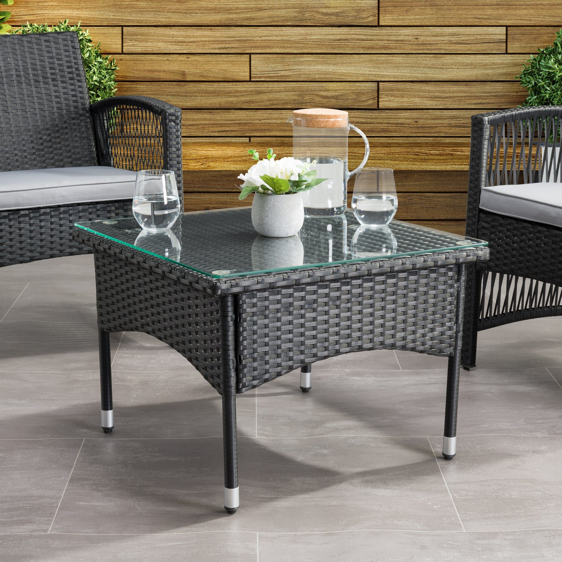 Outdoor wicker side table with glass top, featuring a sturdy metal frame and intricate wicker pattern in brown. Ideal for patio or garden use, offering a stylish and durable addition to outdoor furniture sets.