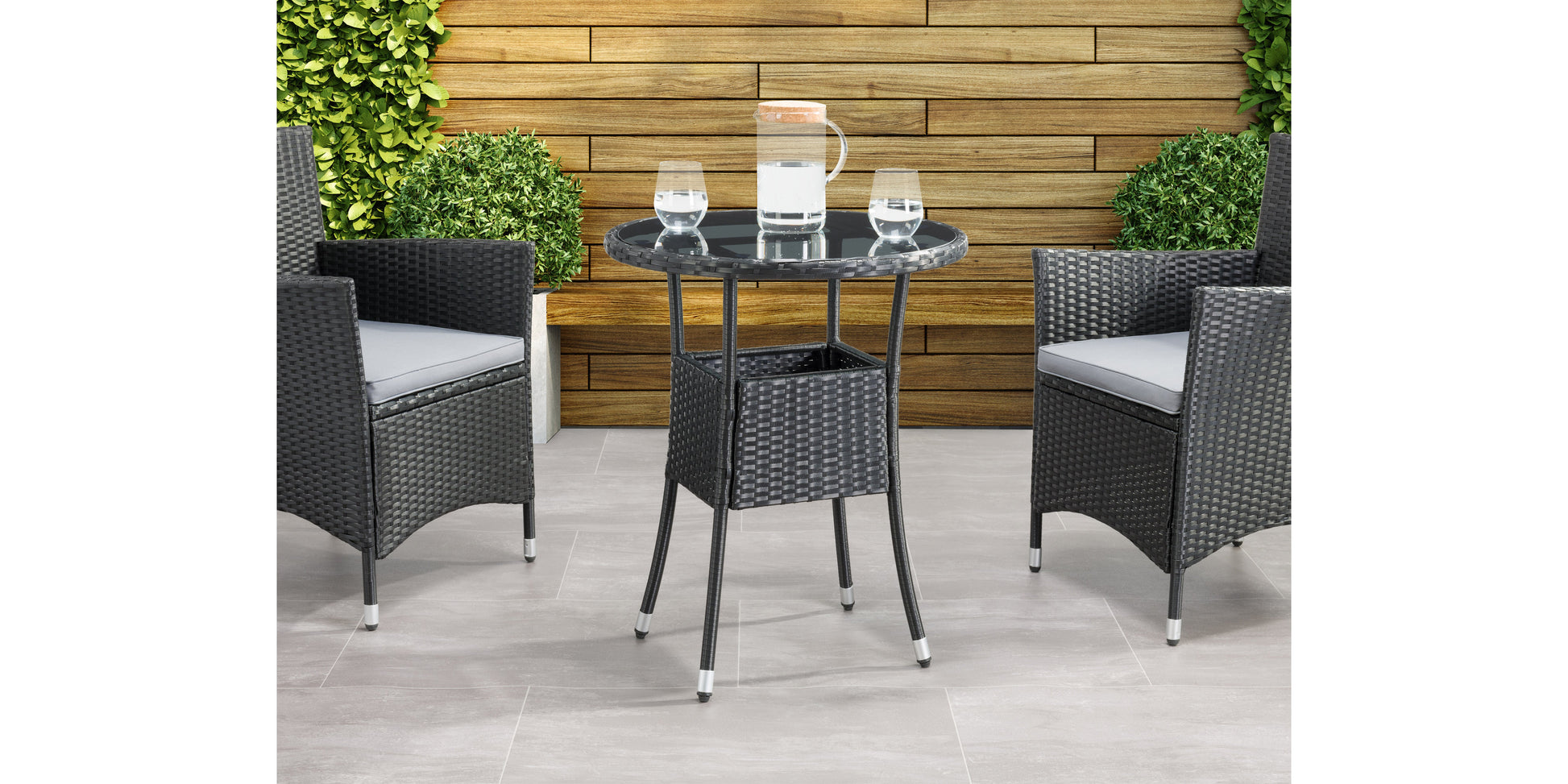 Modern black metal patio bistro table with round top and sleek, minimalist design, set on a wooden deck with greenery in the background. Ideal for outdoor dining and garden decor.